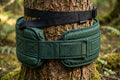 Tree protector strap wraps in green webbing around a cedar tree trunk
